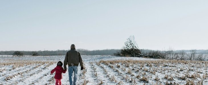 grandfather walks hand in hand with granddaughter on snowy farm