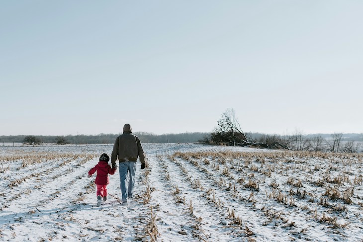grandfather walks hand in hand with granddaughter on snowy farm