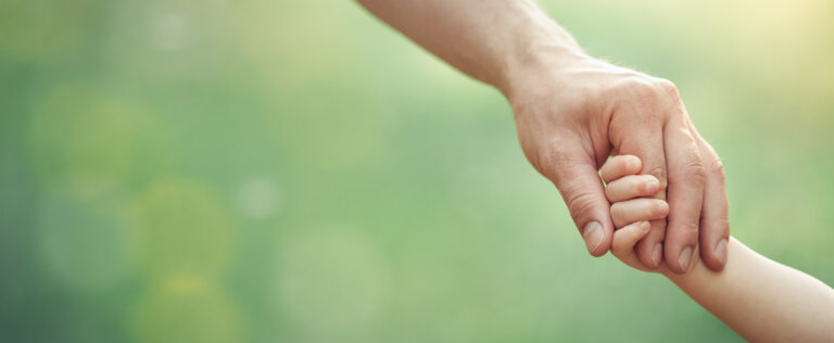 Fathers hand holding his little child in sunny day outdoor, united family and happy childhood concept, banner format with copy space.