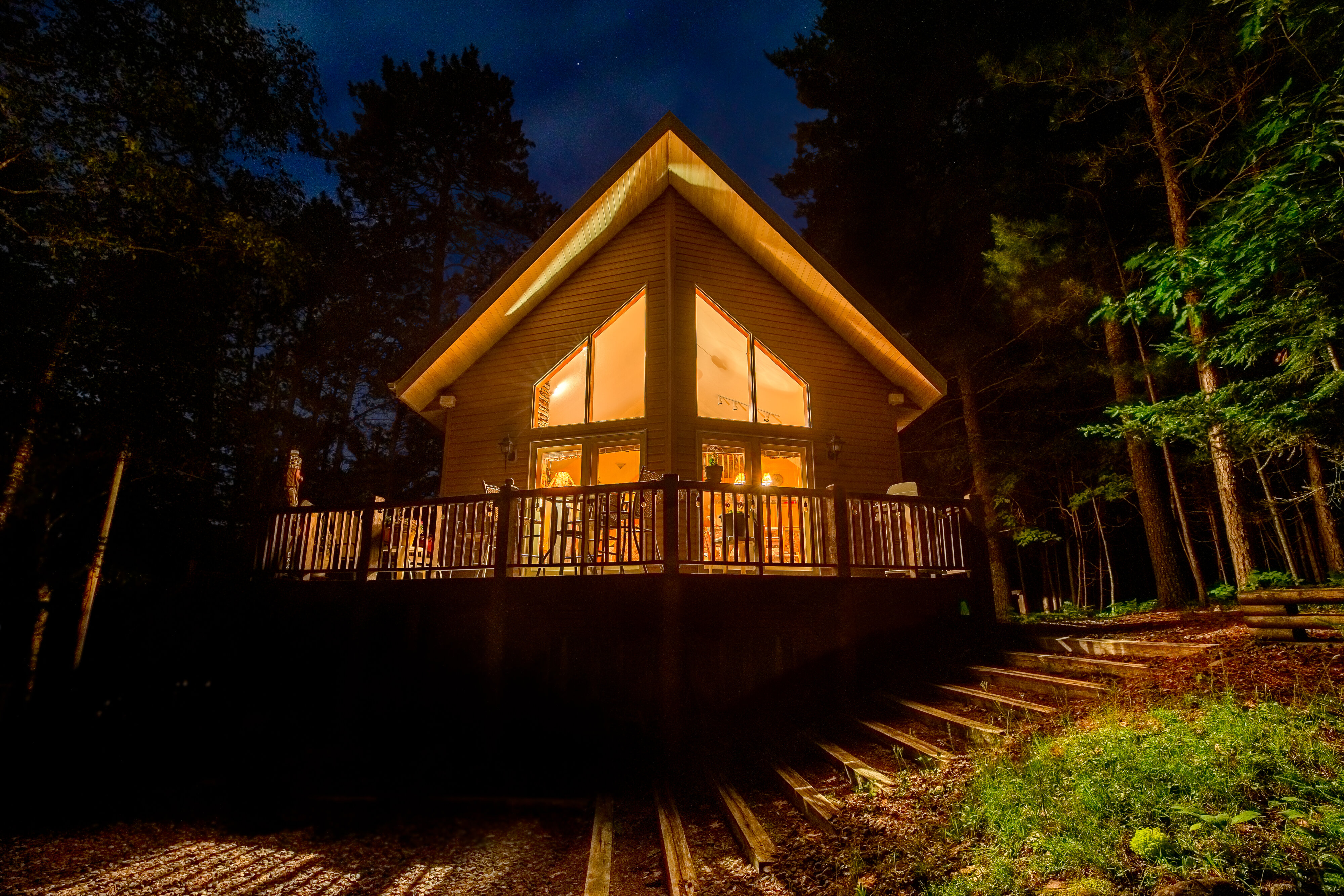 A-frame cabin glowing with warm lights in a forest at night.