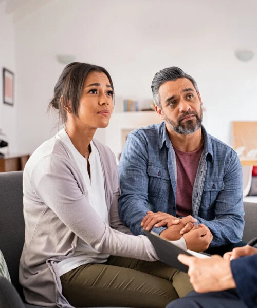 Mature stressed married couple holding hands and talking to advisor